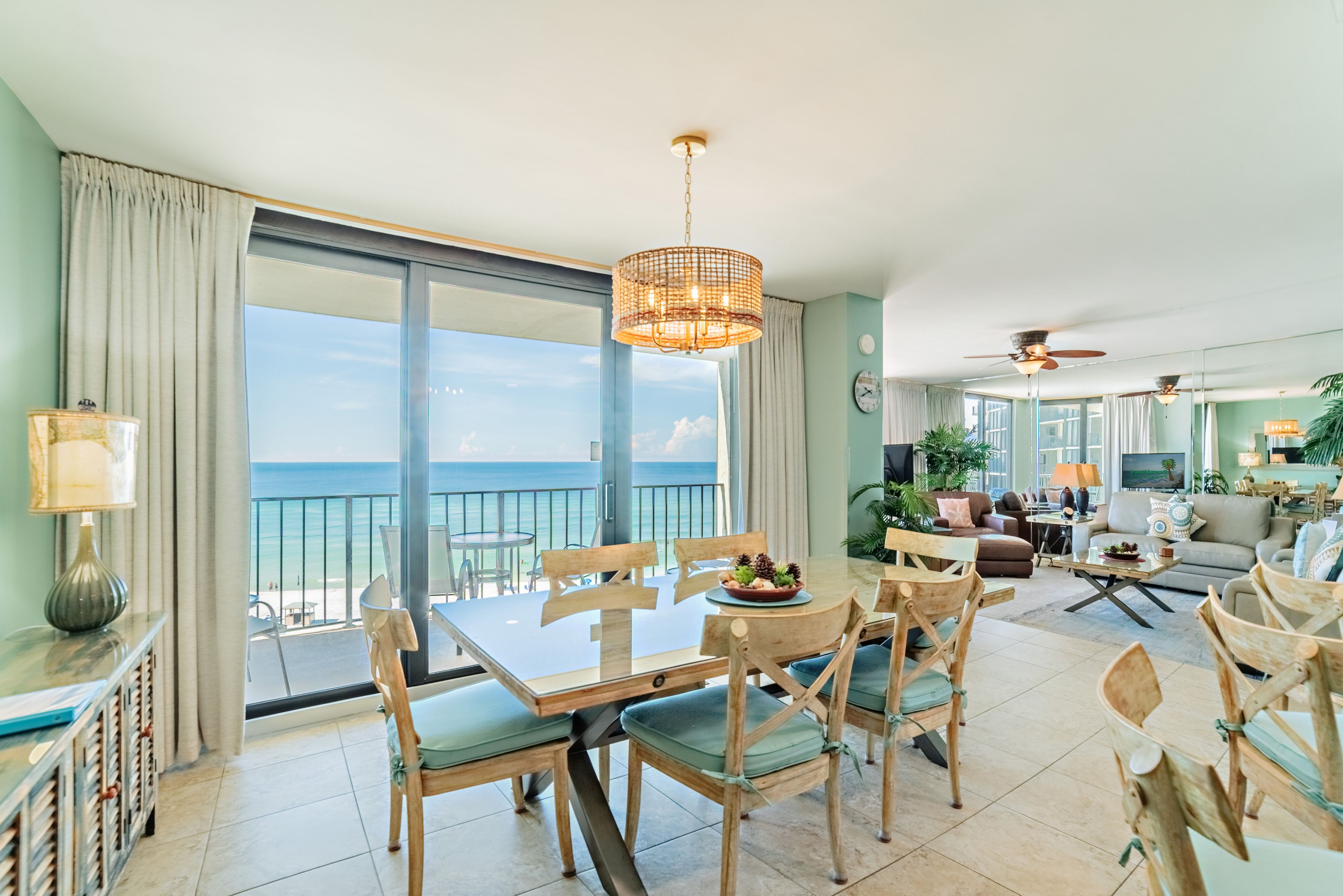 A spacious living area with a balcony overlooking the ocean, furnished with a dining table, chairs, and a television.