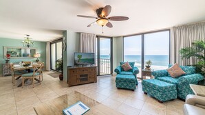 A living room with a dining area, a ceiling fan, a TV, and a view of the ocean.