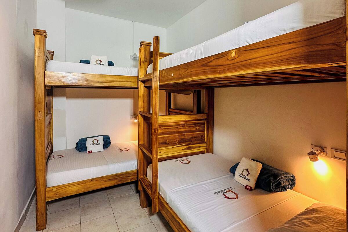 A bunk bed room with a wooden frame, white bedding, and a hanging light fixture.