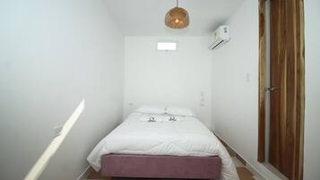 Un dormitorio pequeño y ordenado con una cama individual, un armario de madera, una lámpara colgante y una ventana pequeña.