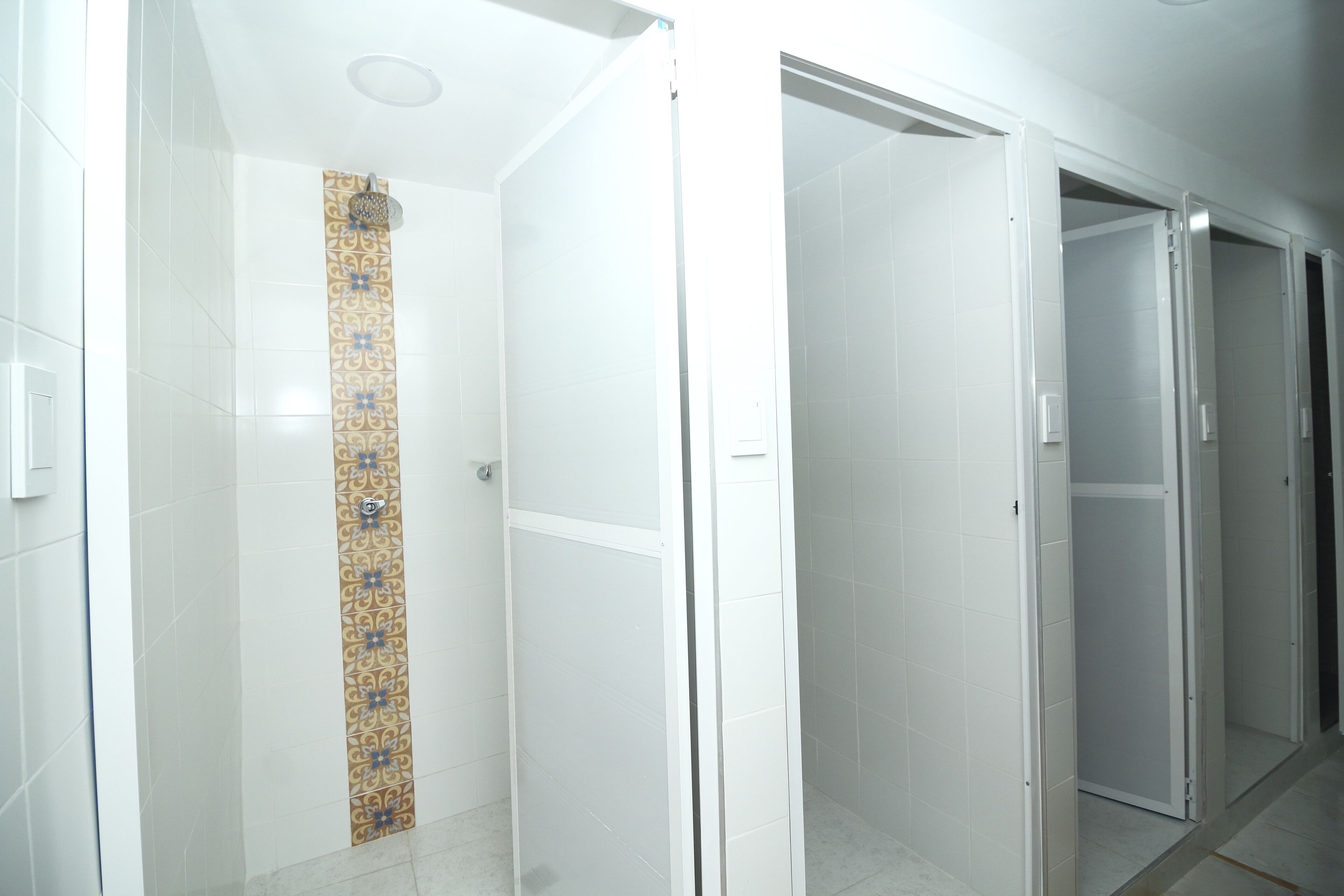 A modern hotel corridor with white walls, a patterned tile column, and a glass door leading to a shower area.