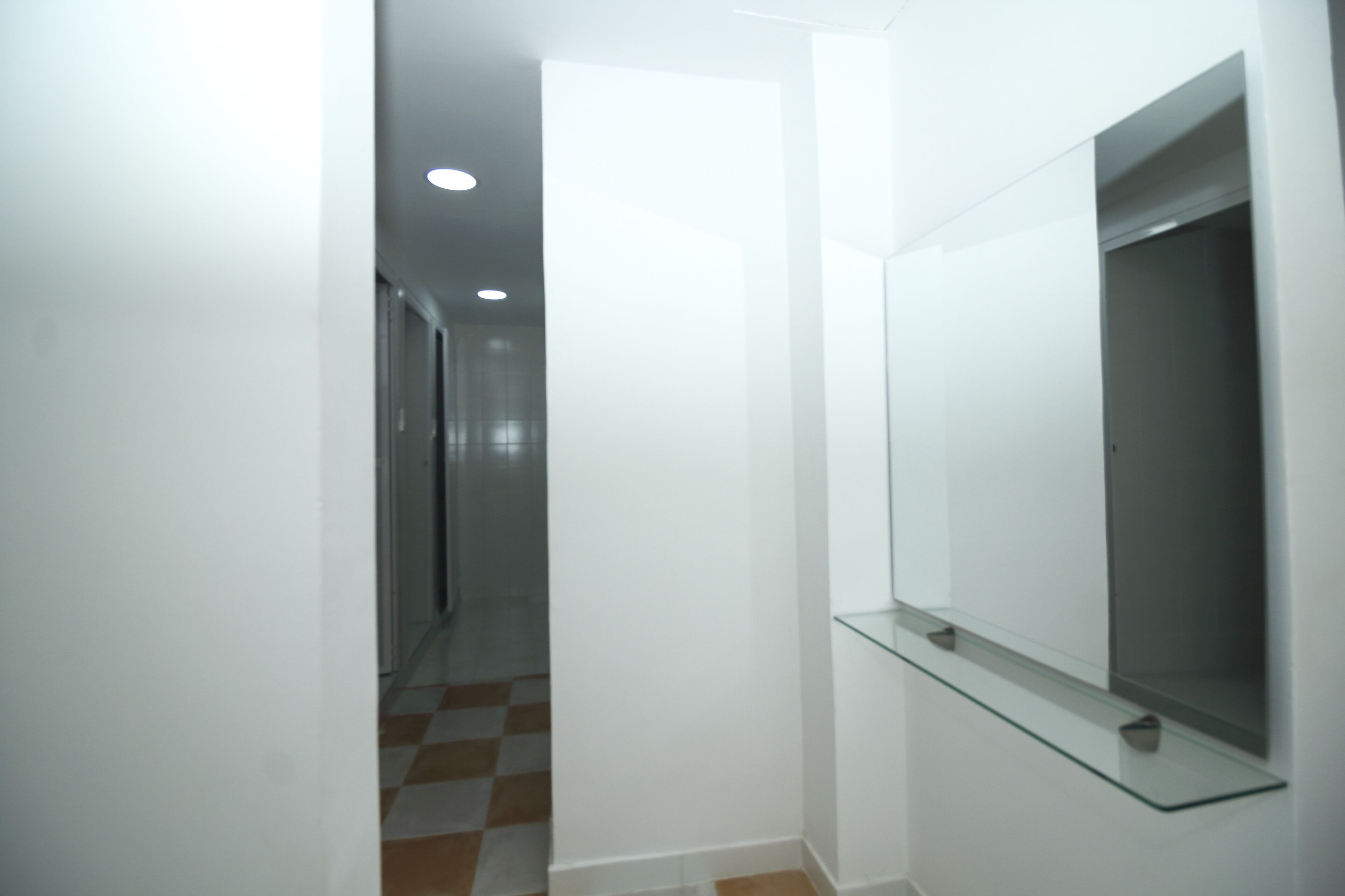 Un couloir étroit avec une étagère en verre et un miroir au mur.