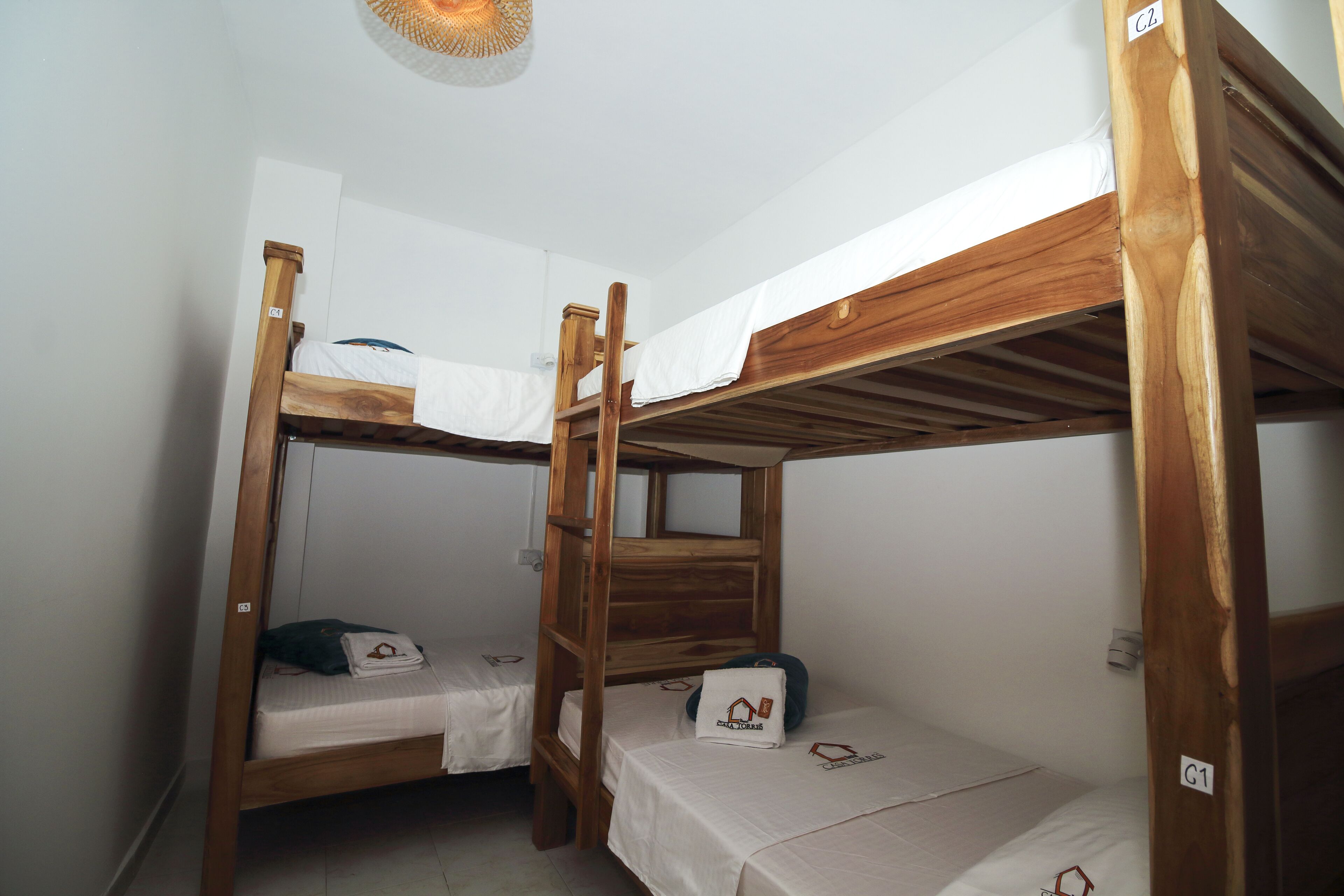A room with two bunk beds, each with a wooden frame and white bedding. There is a small table with a pillow and a pair of glasses on one bed.