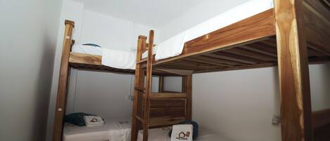 A room with two bunk beds, each with a wooden frame and white bedding. There is a small table with a pillow and a pair of glasses on one bed.