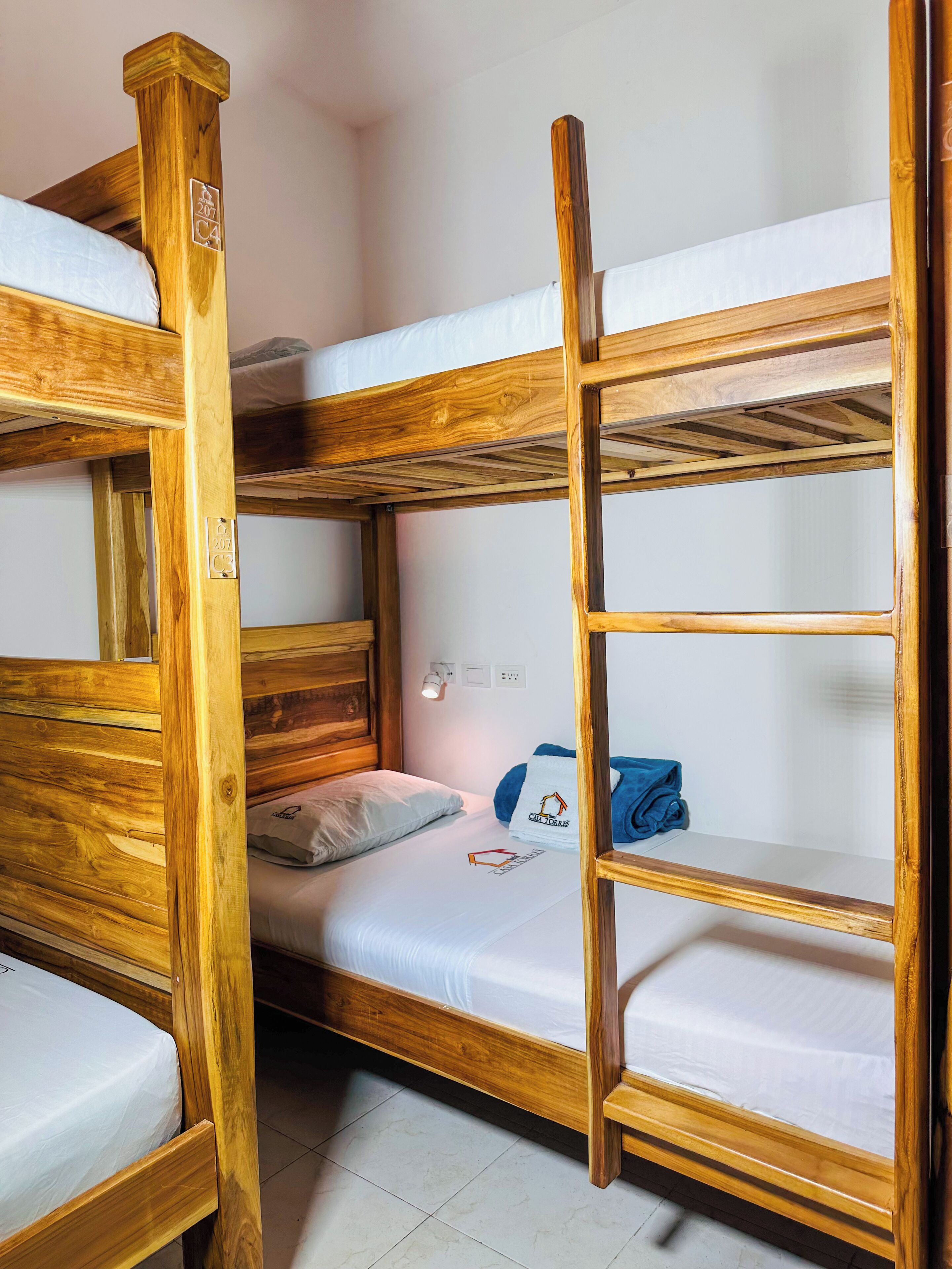 A bunk bed room with wooden frames, a white mattress, a pillow, and a towel on the lower bunk.