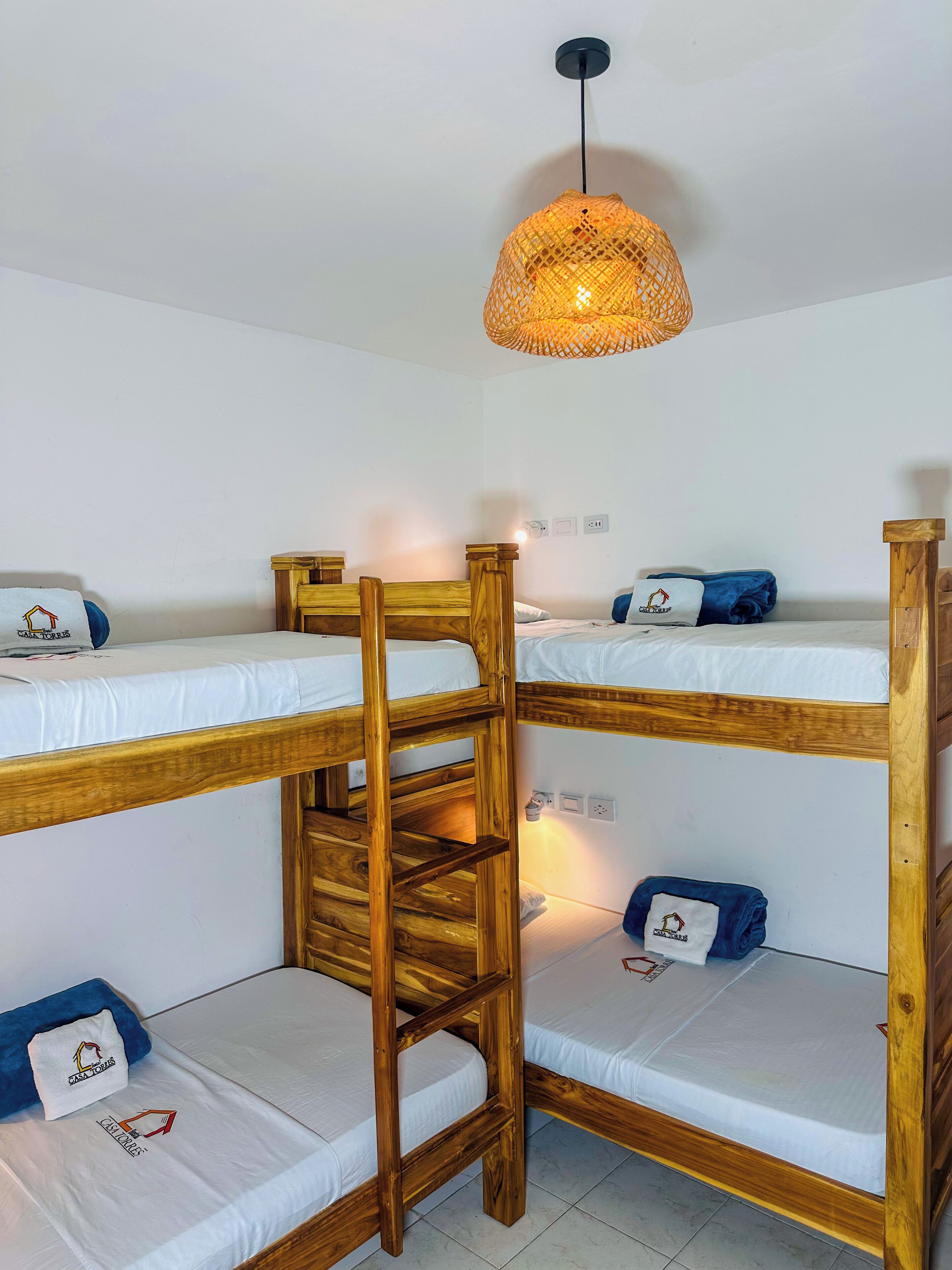 Ein Schlafraum mit Etagenbetten, einer Holzlade, einer gewebten Lampe und einem kleinen Tisch.