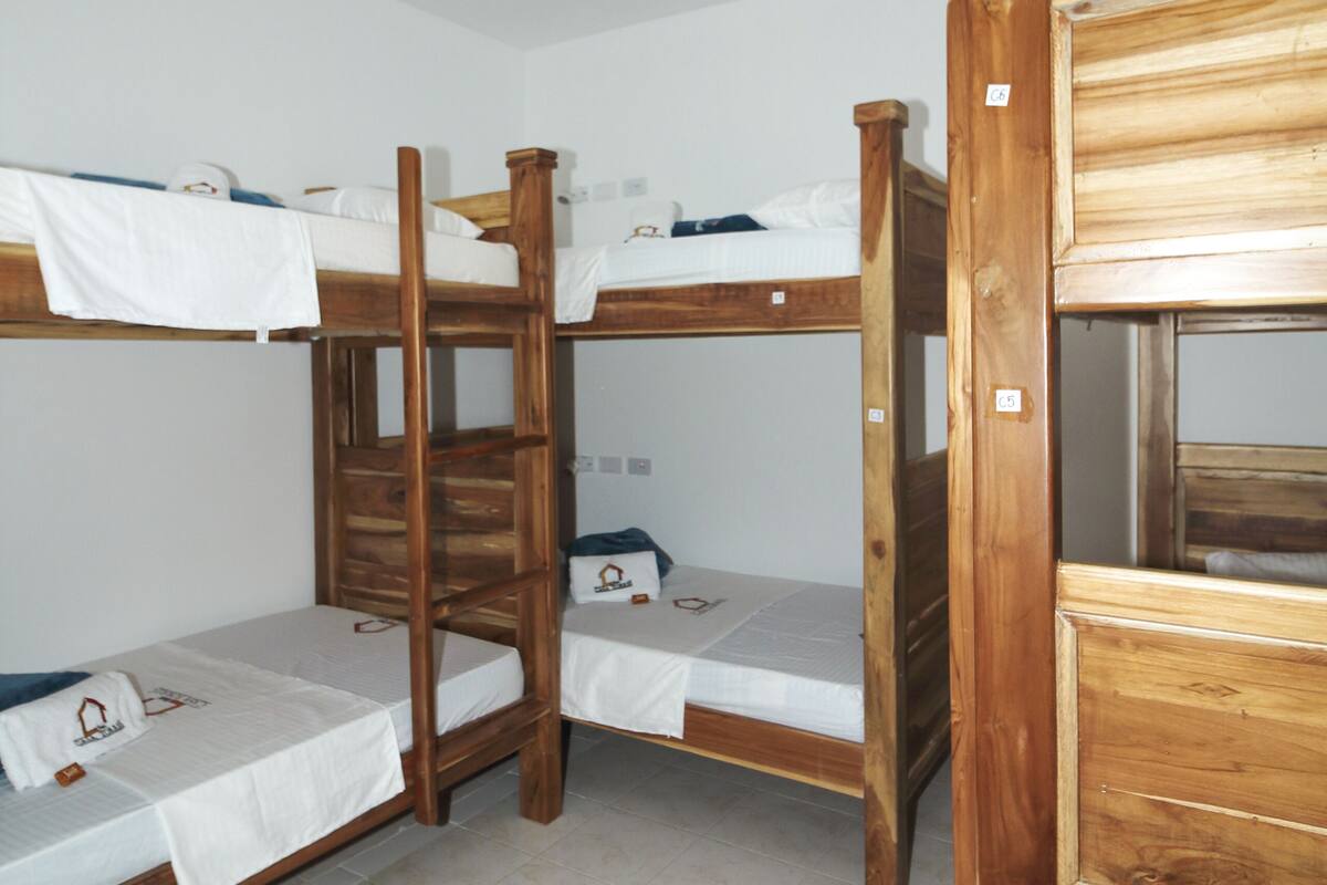 A dormitory room with bunk beds, a wooden wardrobe, and a hanging light fixture.