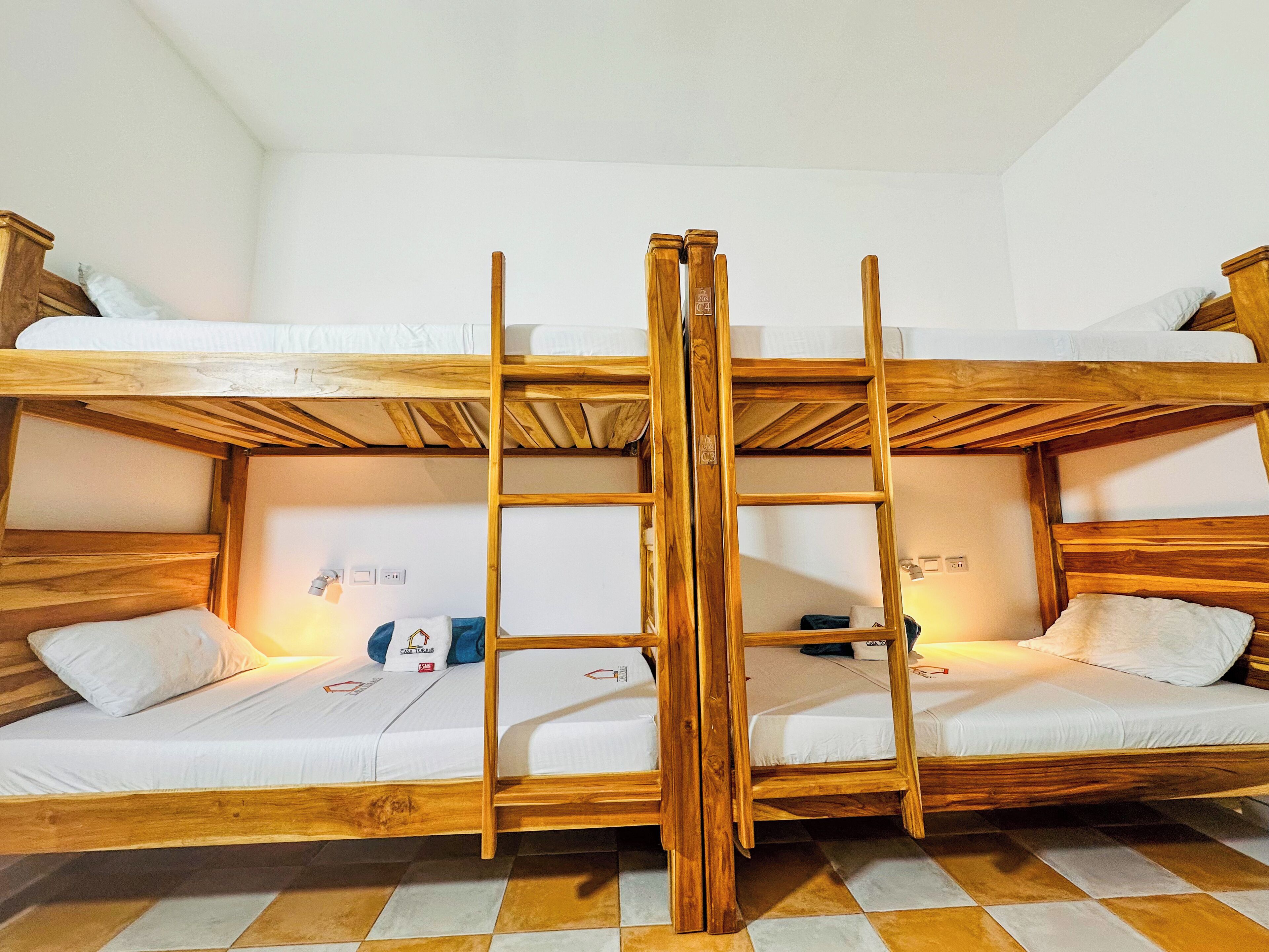 A bunk bed room with a wooden ladder, white bedding, and a checkered floor.