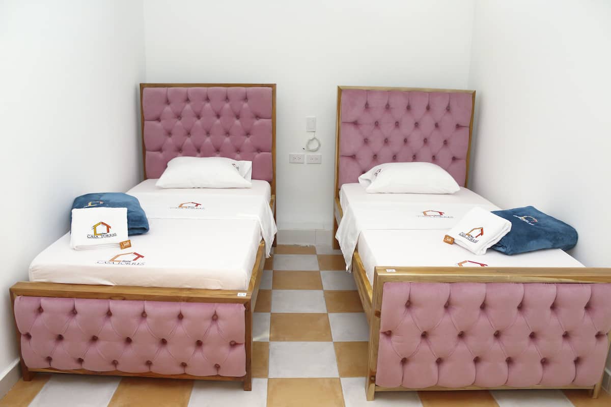 Two twin beds with pink tufted headboards and wooden footboards, white linens, and matching pillows.
