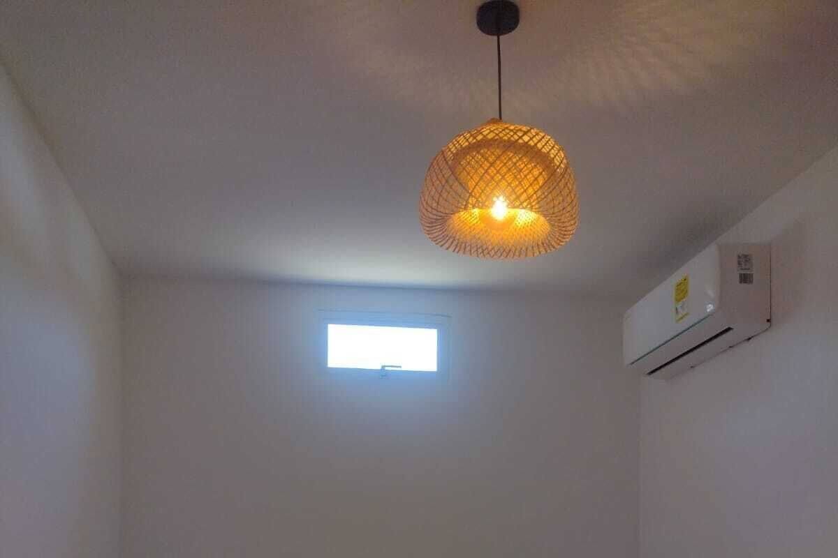 A single bed with white bedding, a small window, and a hanging light fixture.