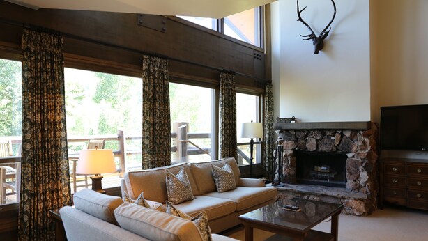 A living room with a stone fireplace, a sofa with decorative pillows, a coffee table, and a mounted deer head on the wall. - Viking Two Bedroom Loft 2 Apartment Hotel by RedAwning (Park City)