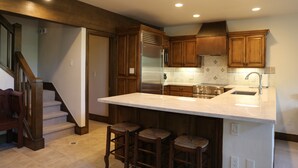A kitchen with wooden cabinets, a stainless steel refrigerator, a large island with stools, and a built-in oven. - Viking Two Bedroom Loft 2 Apartment Hotel by RedAwning (Park City)