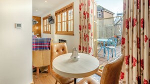 A room with a round table, leather chairs, a television, and a window with curtains.