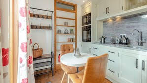 A compact kitchen with a dining area, featuring a round table, chairs, a hanging rack, and built-in appliances.