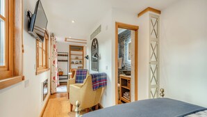 A bedroom with a bed, a chair, a TV, a wardrobe, and a bathroom visible through an open door.