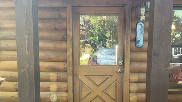 L'ingresso di una baita di legno, con una porta grande, un tappetino d'ingresso e una piccola targa appesa al muro.