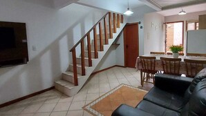 Amplia sala de estar con una escalera que sube a un nivel superior, comedor y televisor de pantalla plana montado en la pared.