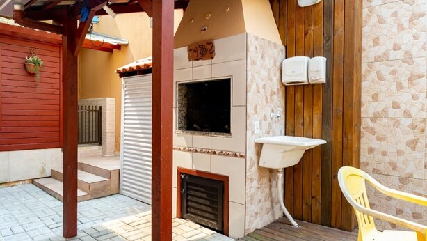 Un patio exterior con pared de piedra, una parrilla y una silla amarilla.