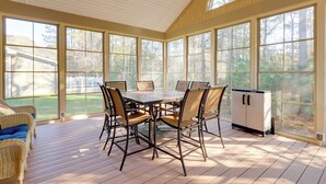 Una sala de estar con ventanales, una mesa grande, sillas, un ventilador de techo y vistas al exterior.