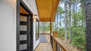 Une terrasse en bois, dotée d’une porte et de fenêtres à cadre noir, donnant sur une zone boisée.
