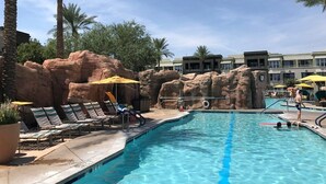 Un espace piscine aménagé avec des chaises longues, des parasols et des palmiers.