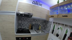 A compact kitchen with a wooden backsplash, a built-in oven, a sink, and a countertop with a knife block. - hébergement au bercail (Beaumont-sur-Sarthe)