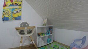 A child's play area with a high chair, a bookshelf with toys, and a play mat. - hébergement au bercail (Beaumont-sur-Sarthe)