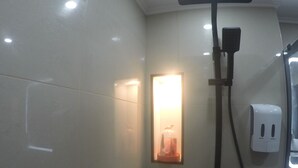 A bathroom with a shower, a wall-mounted light, and a soap dispenser. - hébergement au bercail (Beaumont-sur-Sarthe)