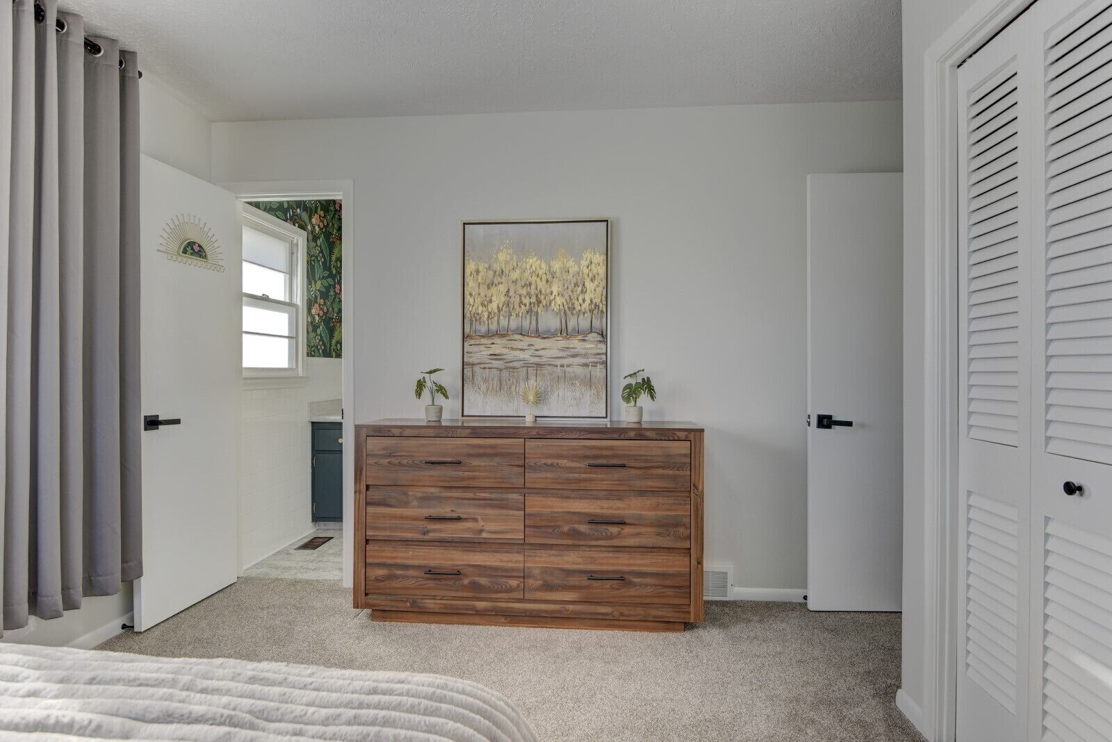 A bedroom with a wooden dresser, a painting, and a bed.