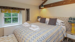 A bedroom with a large bed, a window with a view of greenery, a wooden ceiling, and a bedside table with a lamp. - 3 bedroom accommodation in Broughton, near Skipton (Broughton, near Skipton)