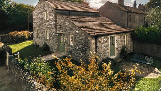A stone house with a sloped roof, a green door, and a small garden with a bench. - 3 bedroom accommodation in Broughton, near Skipton (Broughton, near Skipton)