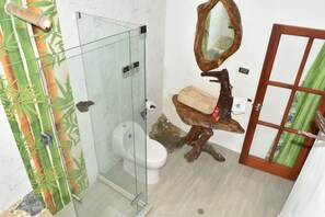 Un baño con cabina de ducha de vidrio, inodoro, lavamanos con base de madera y espejo con marco de madera.