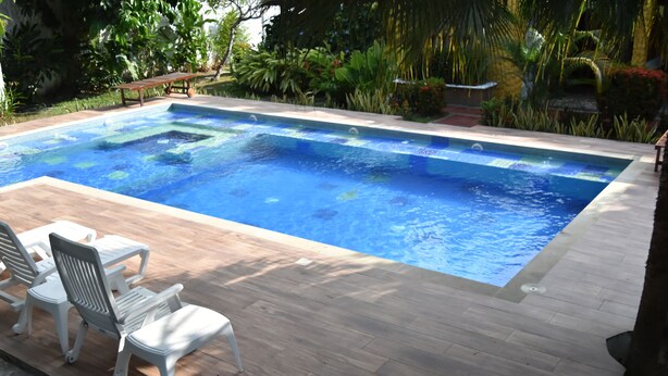 Una piscina rectangular con muelle de madera y sillas de plástico blanco.