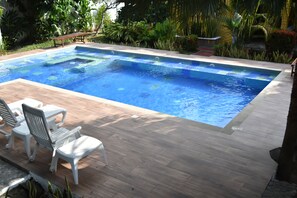 Una piscina rectangular amb una zona de fusta i cadires de plàstic blanc.