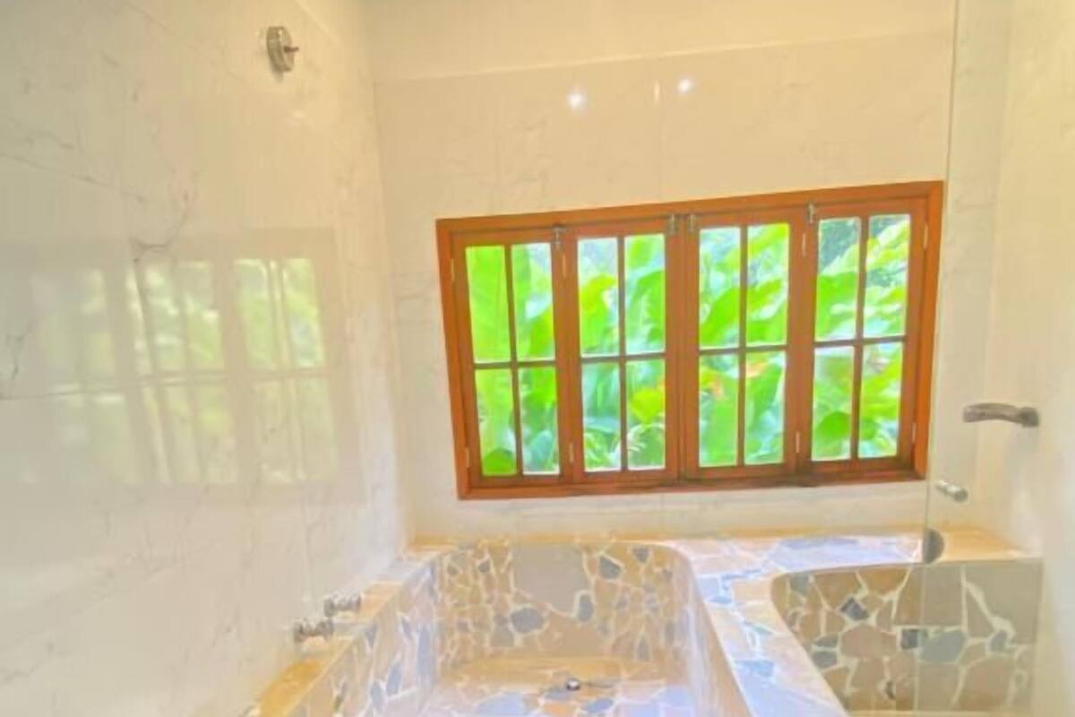 A bathroom with a stone bathtub, a window with a view of greenery, and a shower area.
