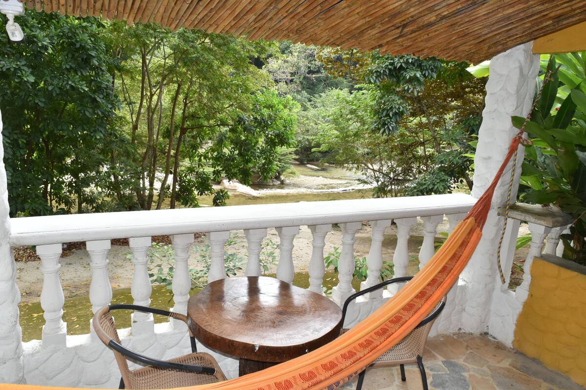 A balcony with a white balustrade, a wooden table, two wicker chairs, and a hammock.
