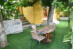 Un patio con una mesa y sillas de madera, rodeado de césped artificial y paredes de piedra.