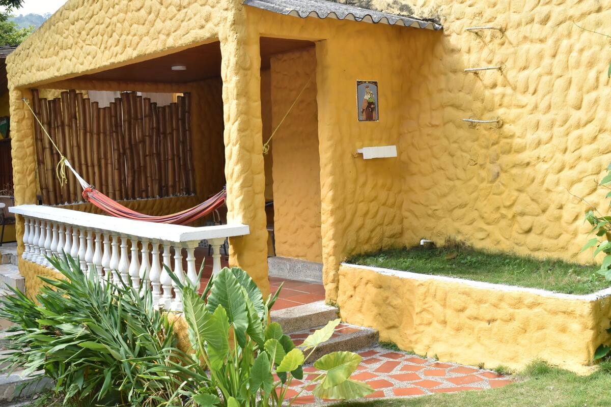 A yellow building with a textured exterior, a hammock, and a small garden area.