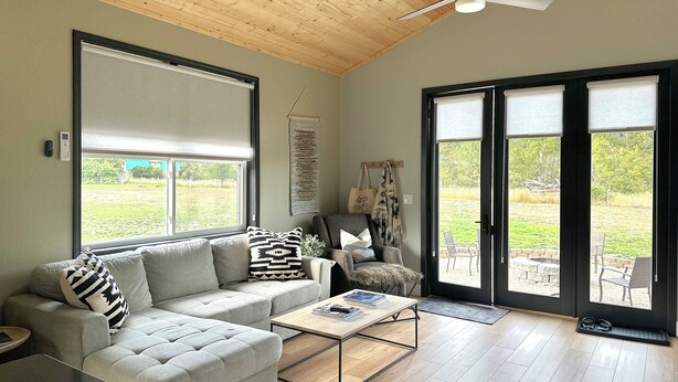 A modern living room with a grey sofa, a coffee table, and a ceiling fan. - Modern,  but cozy apartment with spectacular views of the Bitterroot mountains (Stevensville)