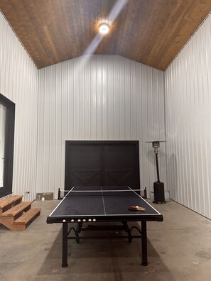 Une table de ping-pong dans une pièce dotée d’un haut plafond en bois et de murs blancs.