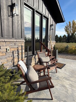 A modern house with a stone exterior, large windows, and a patio with outdoor furniture.