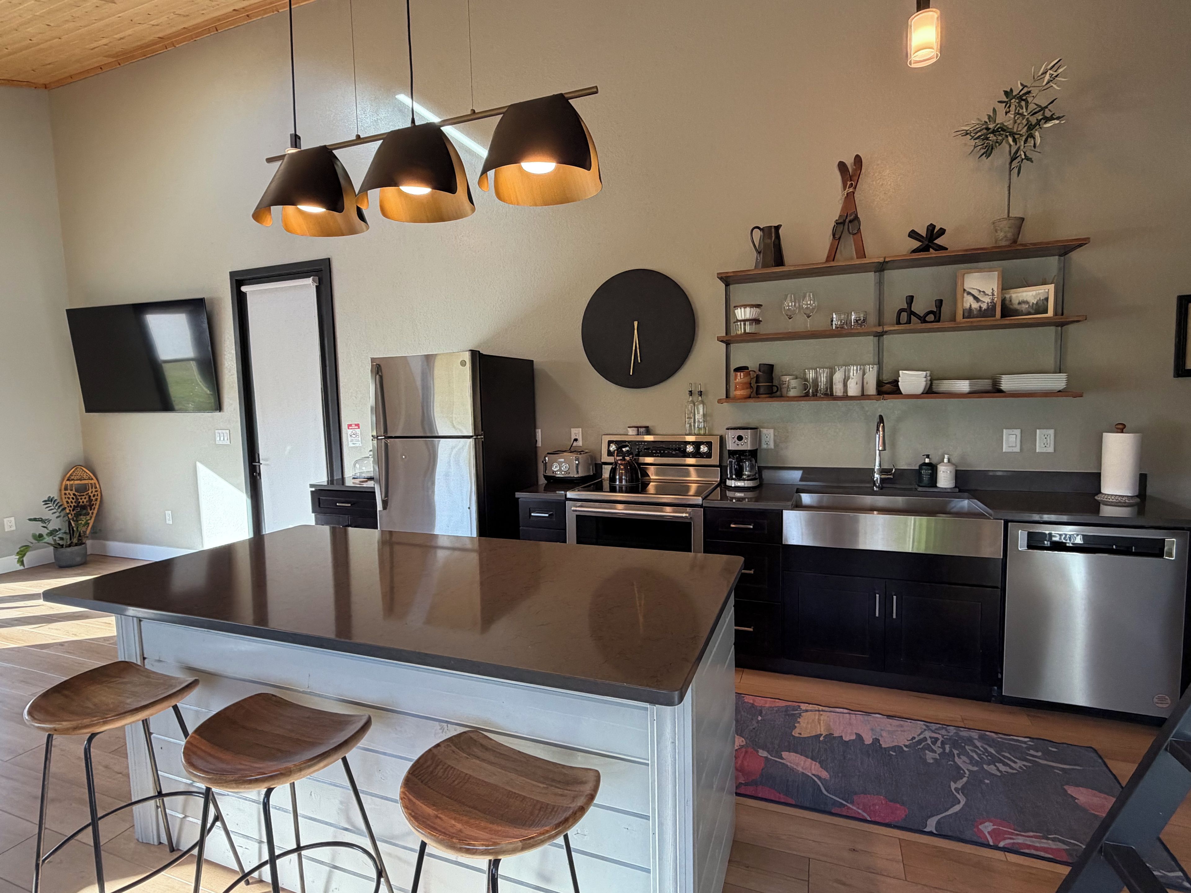 Une cuisine moderne avec un îlot central, des tabourets de bar, des appareils en acier inoxydable et une horloge au mur.