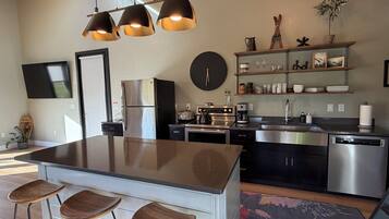 Une cuisine moderne avec un îlot central, des tabourets de bar, des appareils en acier inoxydable et une horloge au mur.