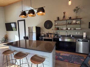 A modern kitchen with a central island, bar stools, stainless steel appliances, and a clock on the wall. - Modern,  but cozy apartment with spectacular views of the Bitterroot mountains (Stevensville)