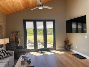 A spacious living room with a large sliding glass door leading to an outdoor area, a ceiling fan, and a flat-screen TV mounted on the wall.