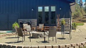 A modern building with a dark exterior, a large glass door, and a patio area with outdoor furniture and a fire pit. - Modern,  but cozy apartment with spectacular views of the Bitterroot mountains (Stevensville)