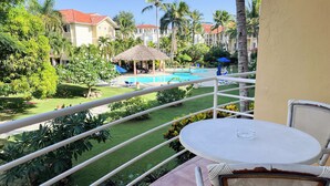 A balcony with a view of a swimming pool, palm trees, and a thatched-roof structure. - Garden view studio, Ocean Front (Cabarete)