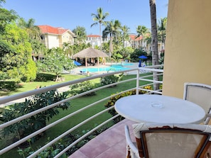 A balcony with a view of a swimming pool, palm trees, and a thatched-roof structure. - Garden view studio, Ocean Front (Cabarete)