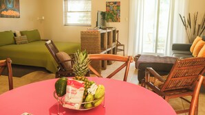 A living room with a green sofa, a wooden chair, a red table with a fruit bowl, and a window with blinds. - Garden view studio, Ocean Front (Cabarete)