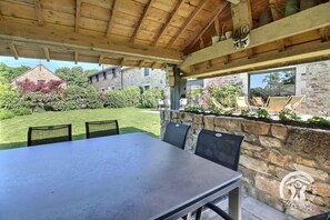 An outdoor covered patio with a stone wall, a table, and chairs.
